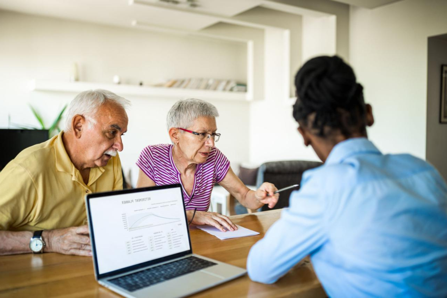 Elder couple speaks to a woman, looking at a computer and paperwork